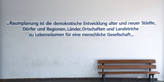 Definition von Raumplanung an der Wand vor dem GB III, eine Bank steht davor