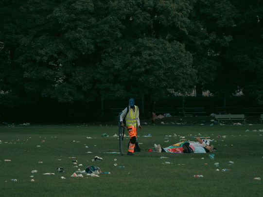 worker picking up garbage next to two people lying down 